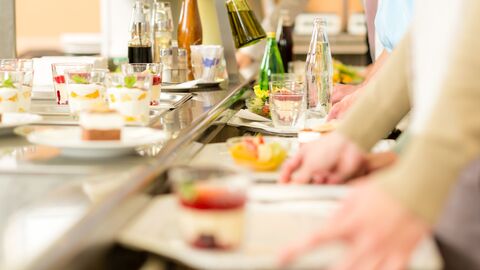 Eine Essensausgabe in einer Mensa; am sieht eine Reihe von Tabletts