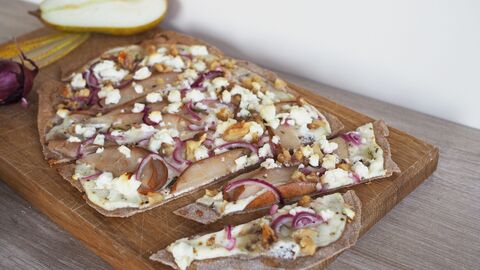 Auf dem Bild sieht man einen Flammkuchen mit Birne und Walnüssen belegt auf einem Holzbrett