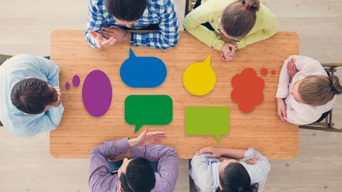 Praxisleitfaden Ein Besprechungsteisch von oben mit bunten Sprechblasen-Bildern