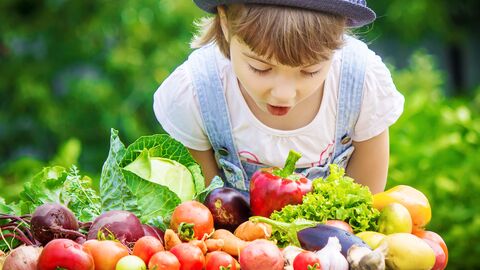 Ein Kind riecht an frisch gepflücktem Obst und Gemüse